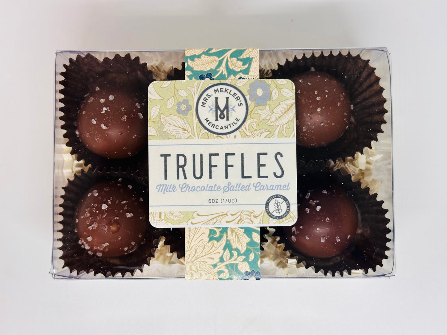 A clear box containing six milk chocolate salted caramel truffles, each truffle covered in a milk chocolate shell sprinkled with coarse salt.