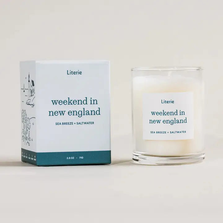 2.5 oz Candle in glass jar and packaging labeled 'weekend in new england' by Literie in light blue and teal stripe on bottom of box