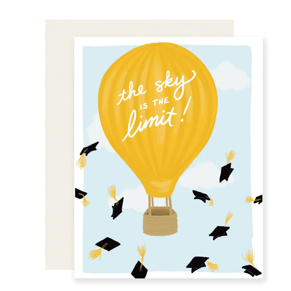 A greeting card with a yellow hot air balloon design and the phrase 'THE SKY IS THE LIMIT!' and falling black graduation caps around bottom
