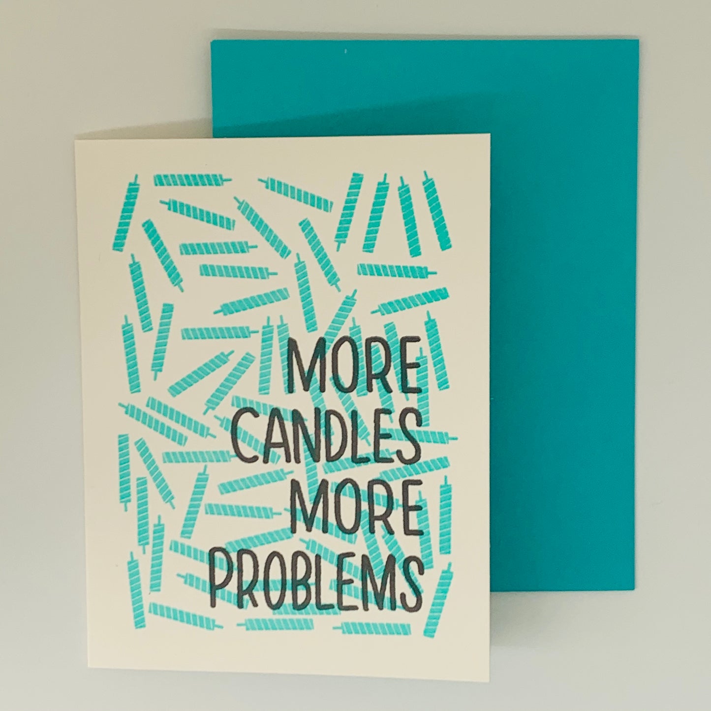 White Greeting Card with the text 'More Candles More Problems' with scattered teal candles. Matching teal envelope