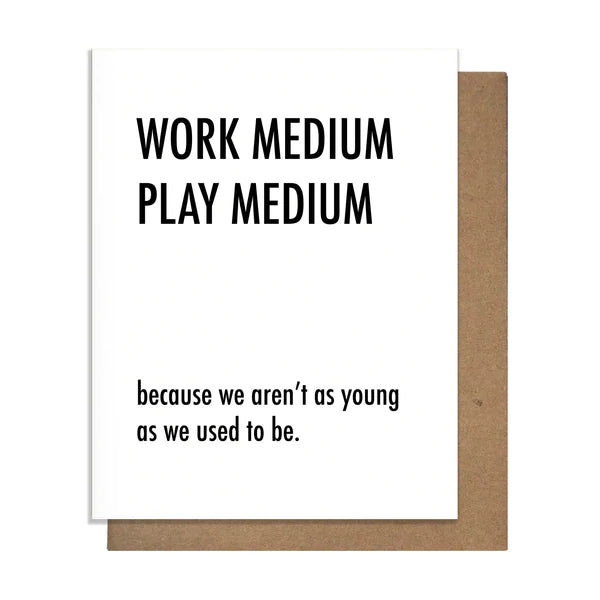 A blank greeting card with the text 'WORK MEDIUM PLAY MEDIUM Because We aren't as young as we used to be' printed on it, accompanied by a kraft envelope.