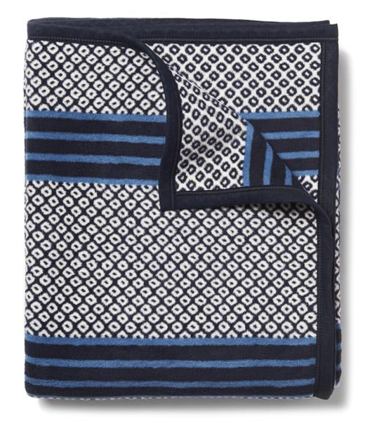 A navy throw blanket with a geometric pattern, featuring blue-on-blue stripes and a New England birdseye pattern.