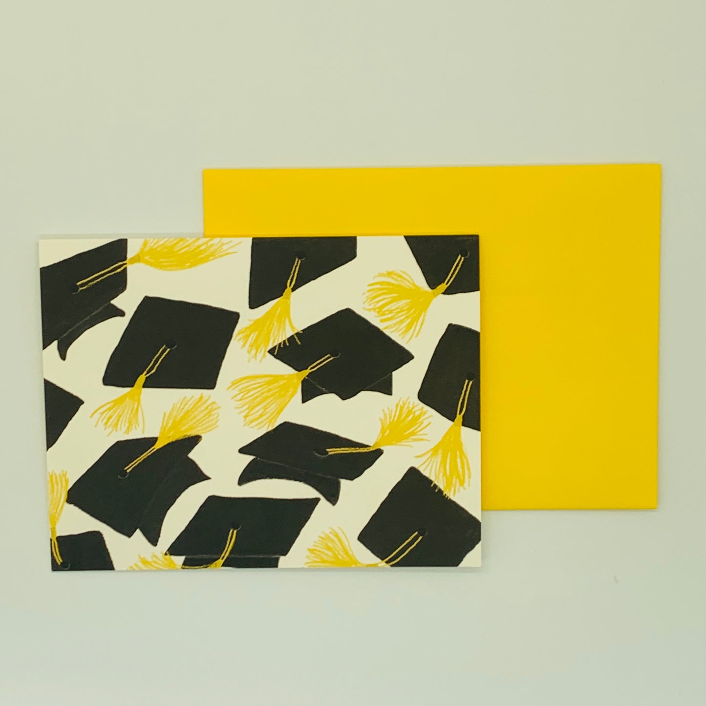 A greeting card with a pattern of black graduation caps and yellow tassels, accompanied by a yellow envelope.