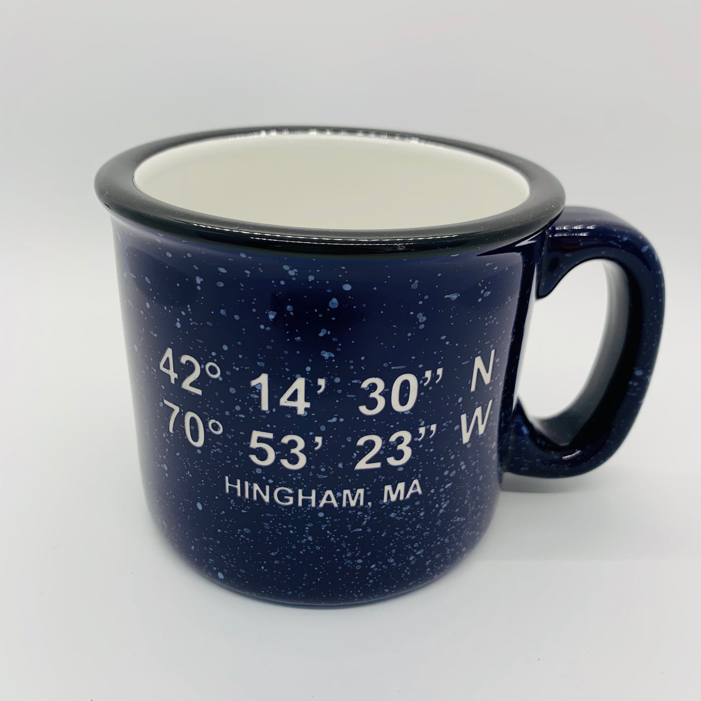 A navy blue ceramic camp style mug with white speckled glaze and geographic coordinate markings for Hingham, MA