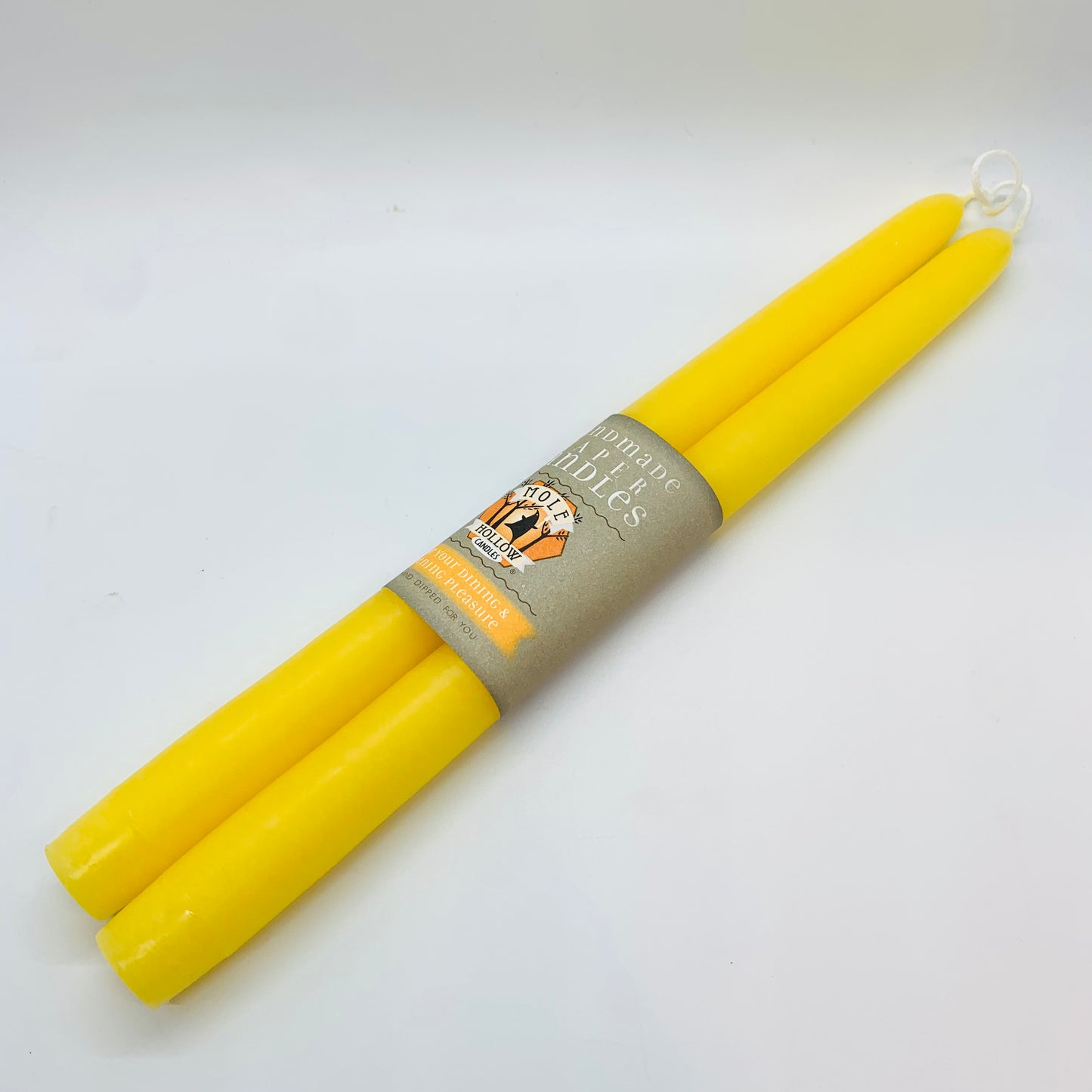 A set of two 12" Sun yellow taper candles , with a label in the middle that has the brand 'Mole Hollow'.