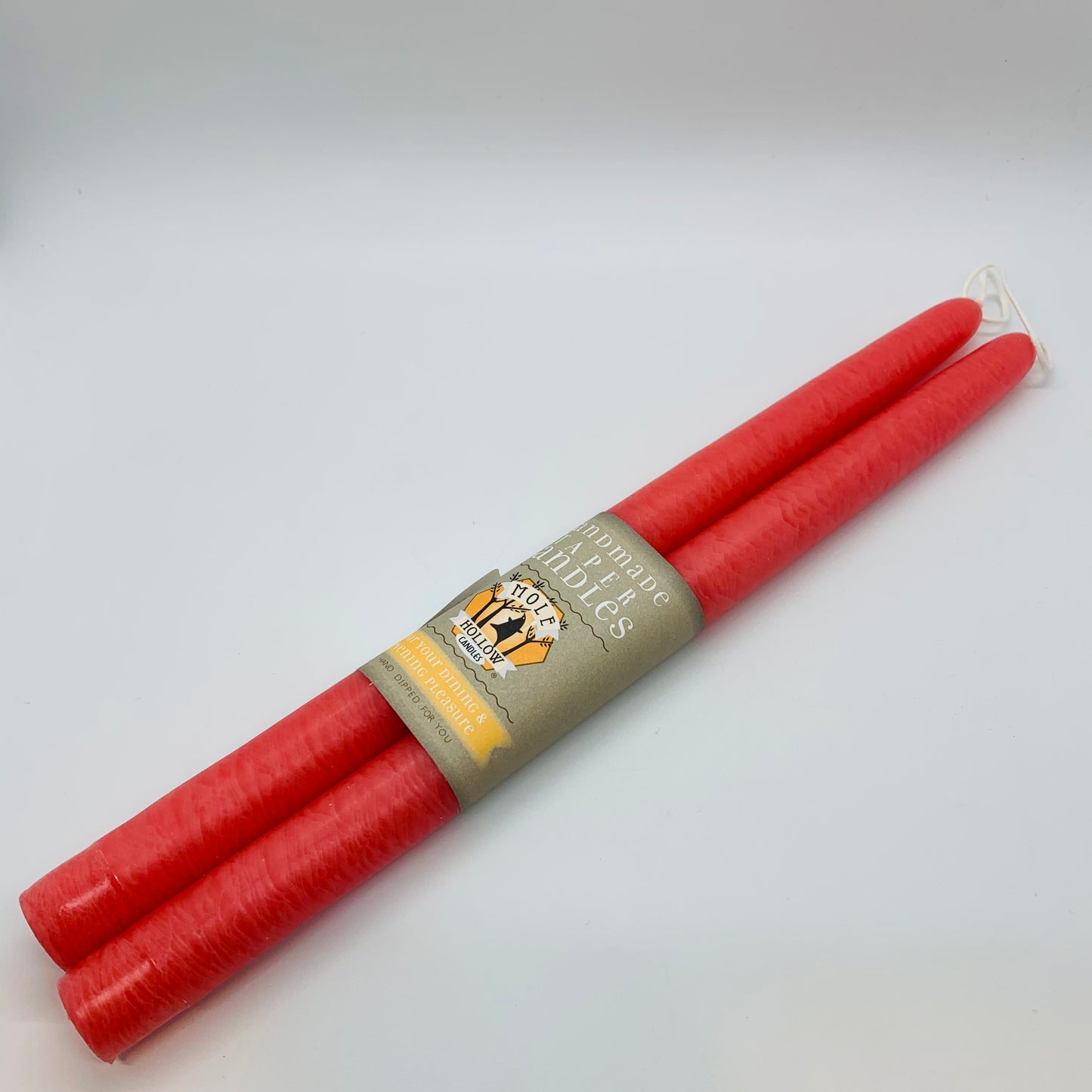 A set of two 12" coral pink taper candles with a label in the middle.