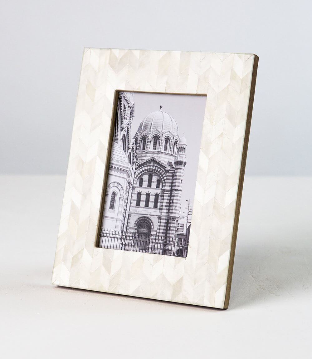 A square picture frame made of bone with a mosaic chevron pattern, holding a 4x6 photo of an architectural building.