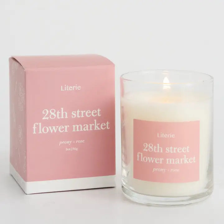 Literie  white candle in glass tumbler with pink label that reads "28th street flower market" in white lettering and pink packaging with same print