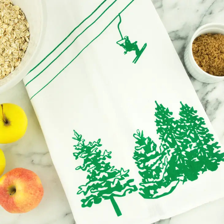  white tea towel with green image of a skier on a chair lift over pine trees 