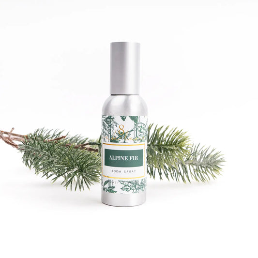 Silver bottle of Alpine Fir room spray with a green label, surrounded by evergreen branches on a white background.