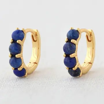 Gold hoop huggie earrings with blue lapis stones on a light gray background