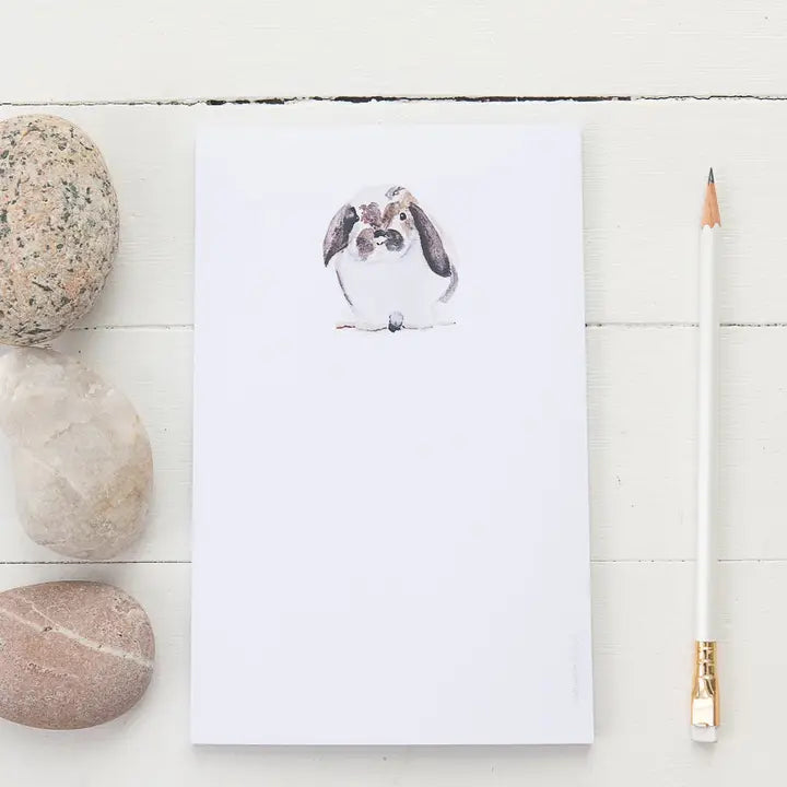 Notepad with a bunny illustration on a white wooden surface with stones and a pencil.