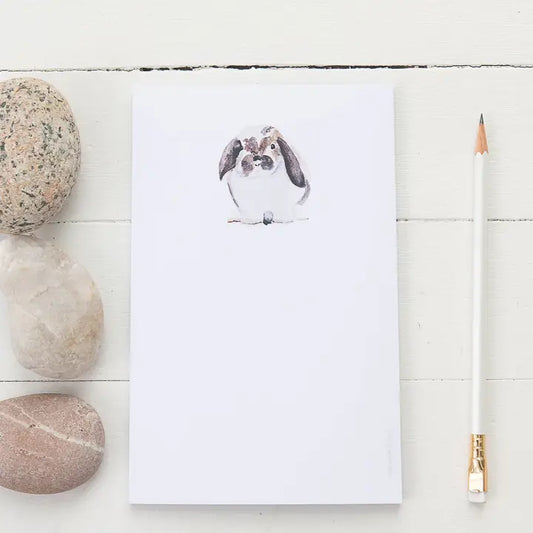 Notepad with a bunny illustration on a white wooden surface with stones and a pencil.
