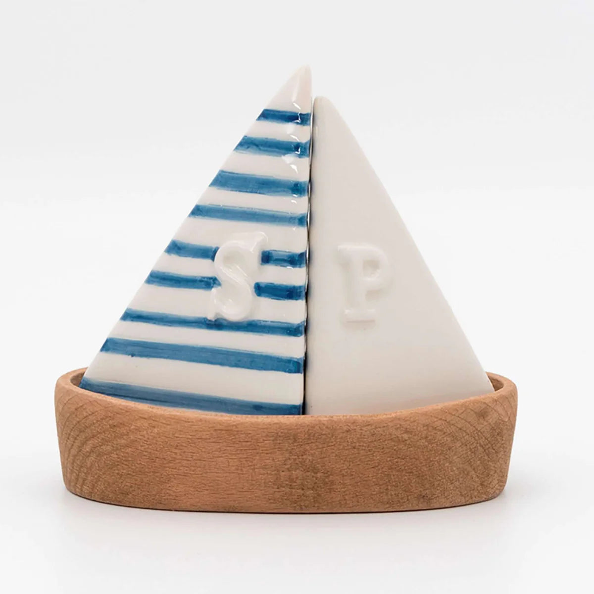 A set of sailboat-shaped salt and pepper shakers with a solid white ceramic sail and navy blue and white striped ceramic sail, placed on a wooden boat shaped base