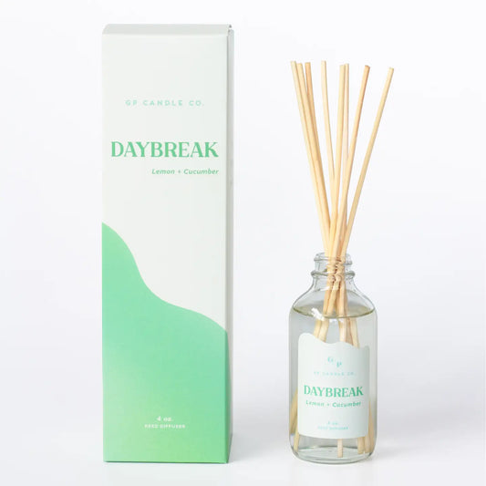 A reed diffuser bottle with natural reeds next to its white and mint green packaging box, labeled 'GP CANDLE CO. DAYBREAK Lemon + Cucumber'.