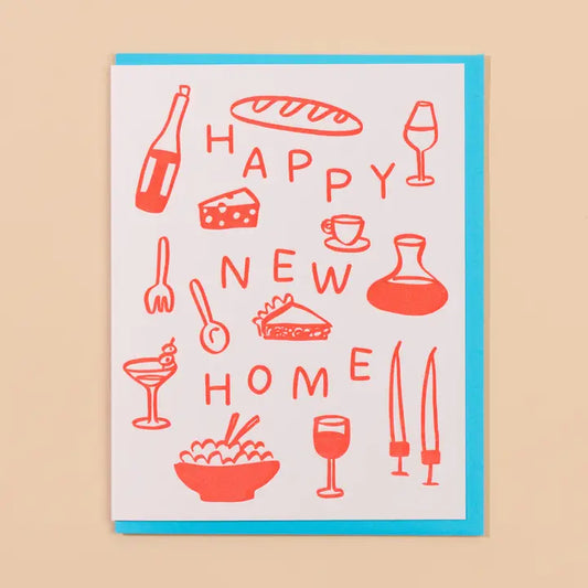 A greeting card with a white background and a bright turquoise envelope, printed with coral-red line drawings of a loaf of bread, wine, cheese, candles and more, and the words “HAPPY NEW HOME.”