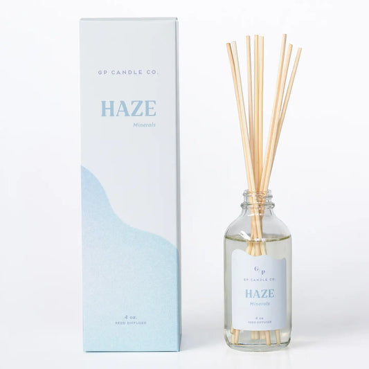 GP Candle Co. Haze Minerals reed diffuser with a clear glass bottle, natural wood reeds, and a white and light blue box next to it on a white background.