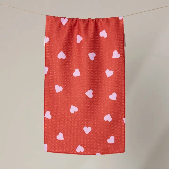 Red towel with pink heart patterns hanging on a line against a beige background
