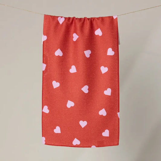 Red towel with pink heart patterns hanging on a line against a beige background