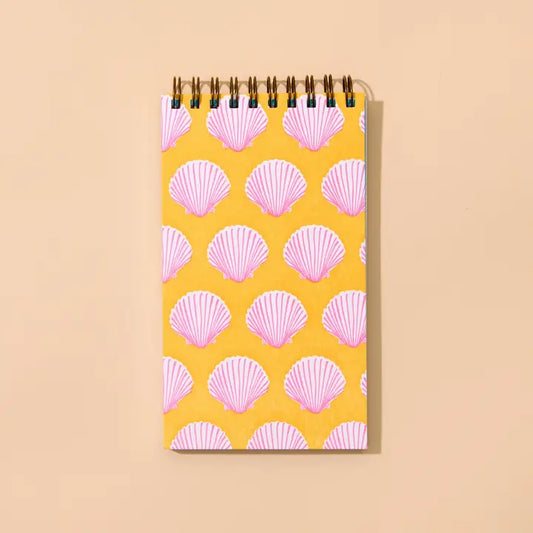 A spiral-bound notebook with a yellow cover decorated with a repeating pink scallop seashell pattern.