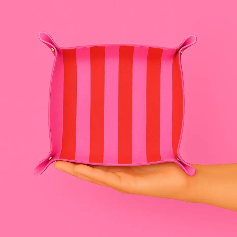 Pink and red striped leather tray held in a hand against a pink background