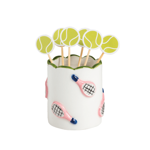 Tennis-themed toothpick holders with tennis ball picks in a scalloped ceramic holder with pink rackets scattered over it 