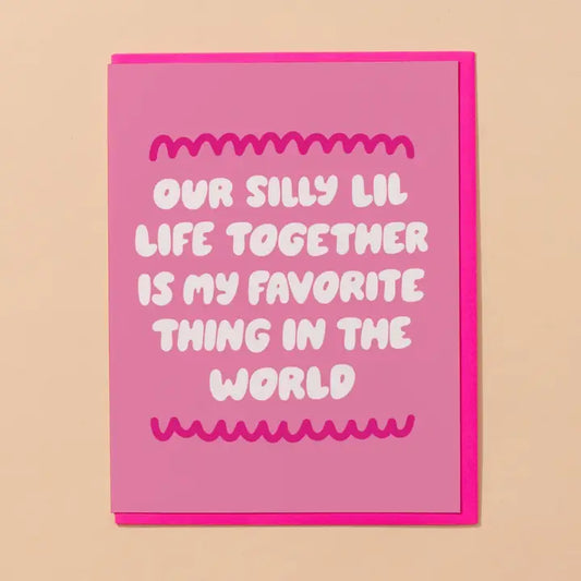 A pink greeting card with a bright pink envelope, featuring the text 'OUR SILLY LIL LIFE TOGETHER IS MY FAVORITE THING IN THE WORLD' in white hand-drawn letters.