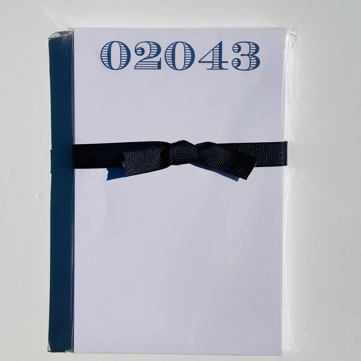 White Notepad with 02043 on top in navy white stripes.  Notepad has a navy bow around it