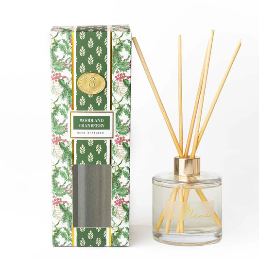 Woodland Cranberry reed diffuser shown with its patterned retail box and the glass diffuser bottle containing natural reed sticks, on a clean white background. The packaging has repeating sprigs of holly berry as well as a green and white block print stripe down the center.