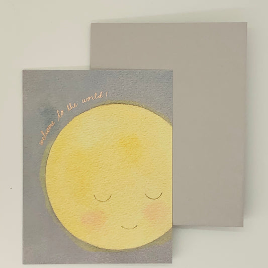 A new baby greeting card with an illustration of a smiling moon on the front, with the text 'welcome to the world'