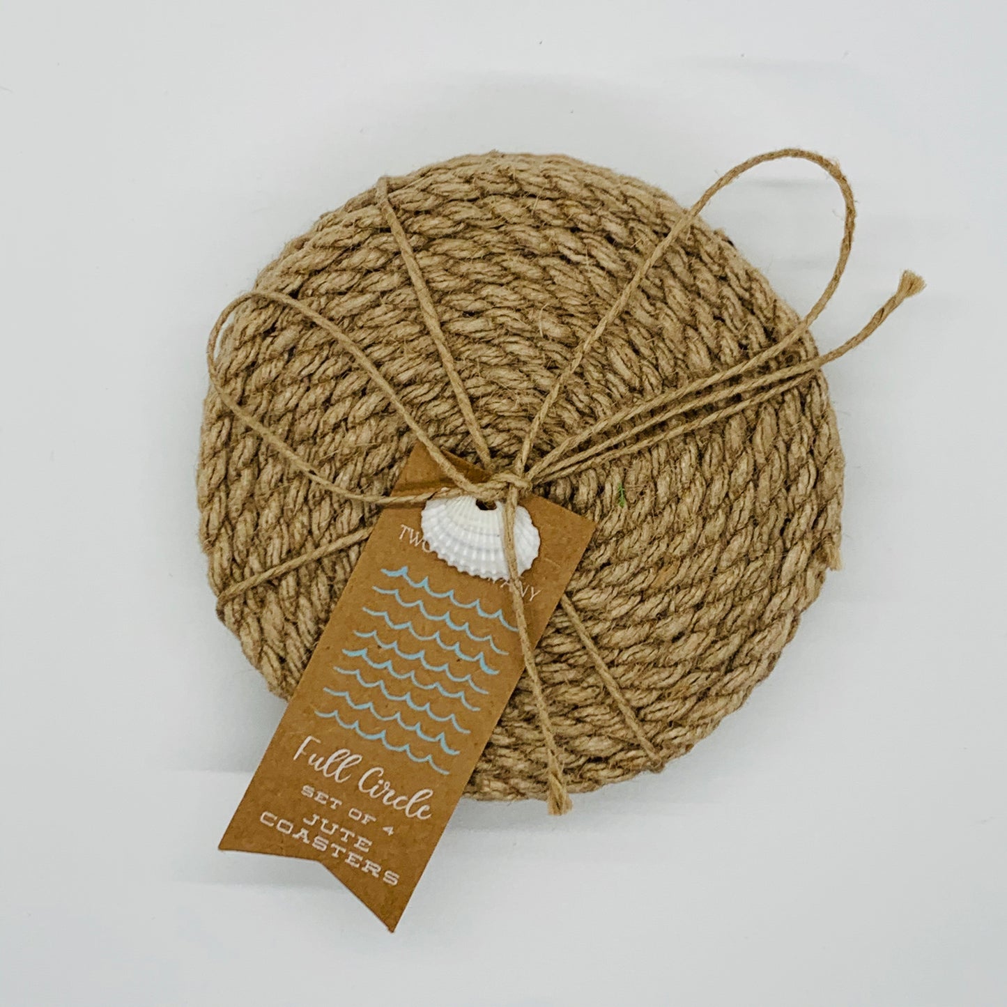 A round jute coaster made of rope with a fabric bottom, displayed on a flat surface. It is primarily beige in color and has a tag with the brand name 'Full Circle' attached to it.