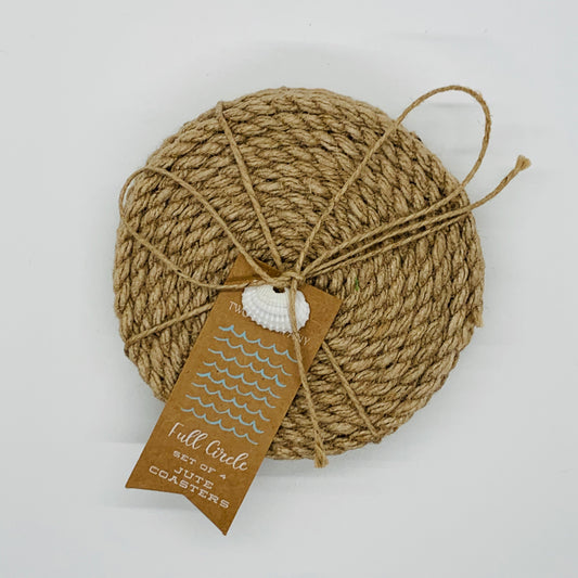 A round jute coaster made of rope with a fabric bottom, displayed on a flat surface. It is primarily beige in color and has a tag with the brand name 'Full Circle' attached to it.